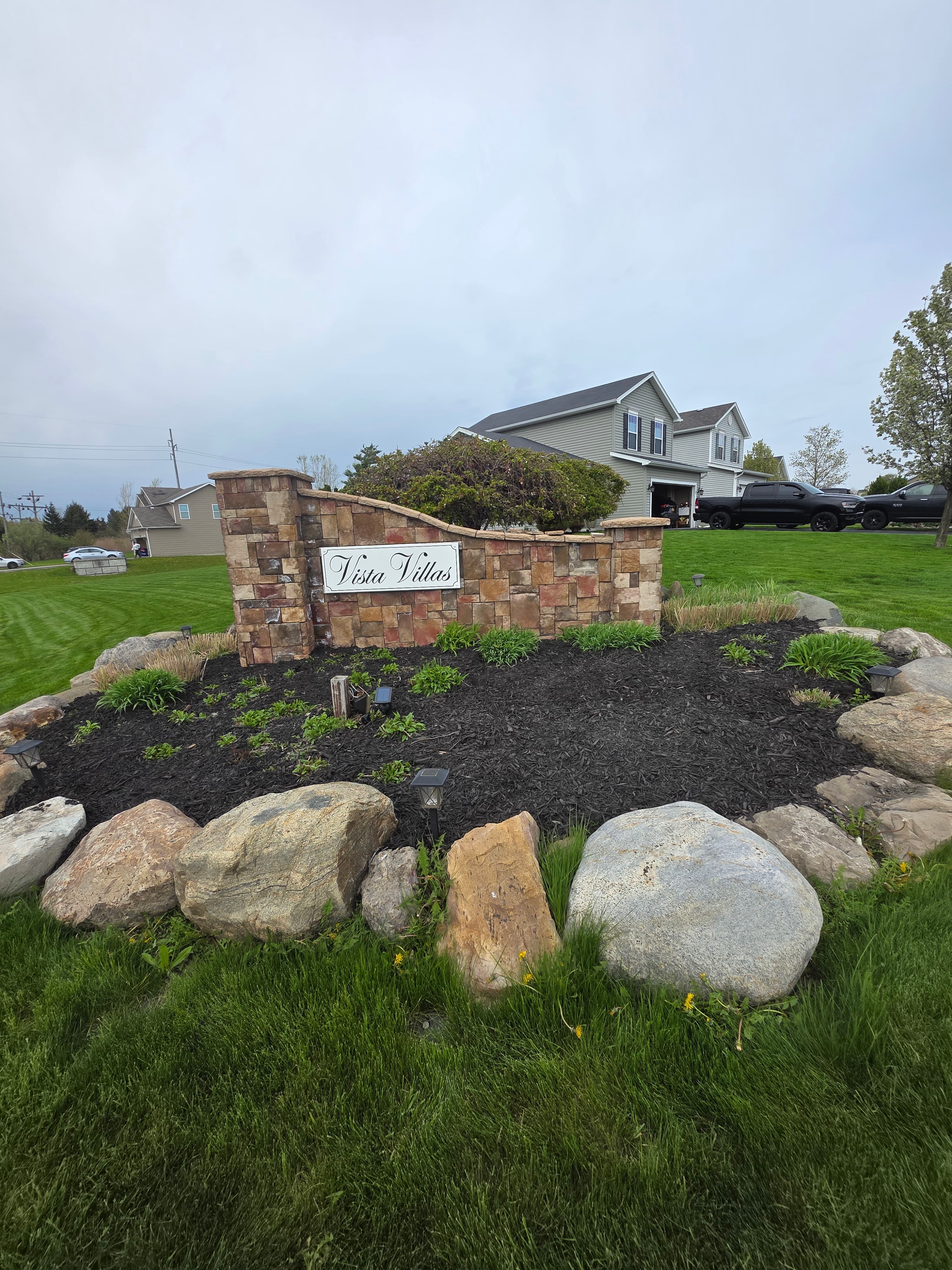 Stone entrance sign for Vista Villas surrounded by mulch, large boulders, and green grass.