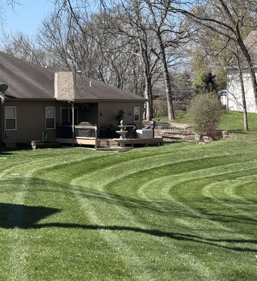 Manicured green lawn with curved mowing stripes leading toward a house with a wooden deck.
