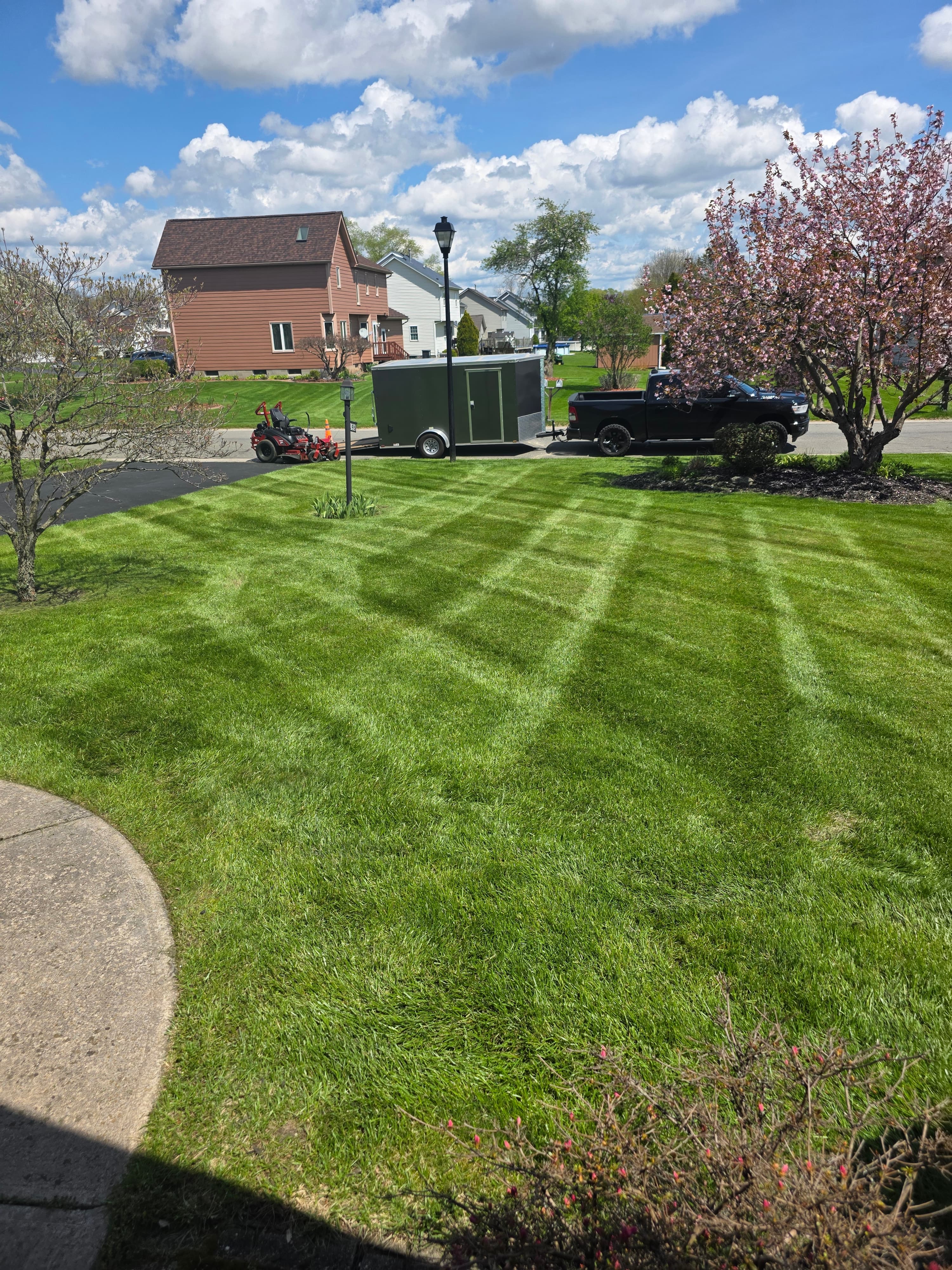 Manicured lawn with diamond stripes, a black truck towing a trailer, and suburban houses.
