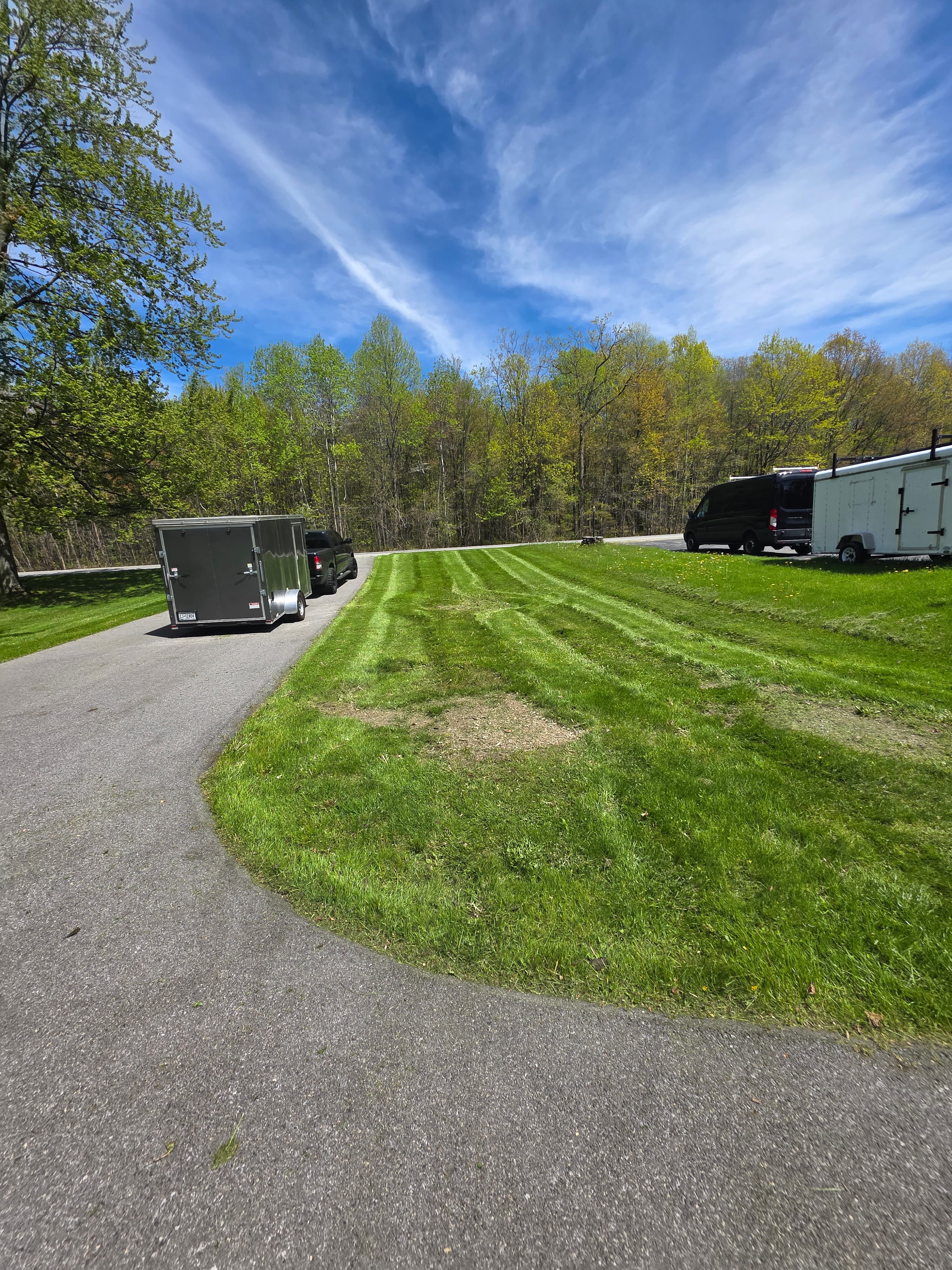 A grey trailer parked on a driveway beside a freshly mowed lawn with visible stripes.